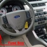 Passenger compartment fuse box location in a 2010 Ford Focus, situated below the steering wheel and to the left of the brake pedal, after removing the under-steering wheel cover.